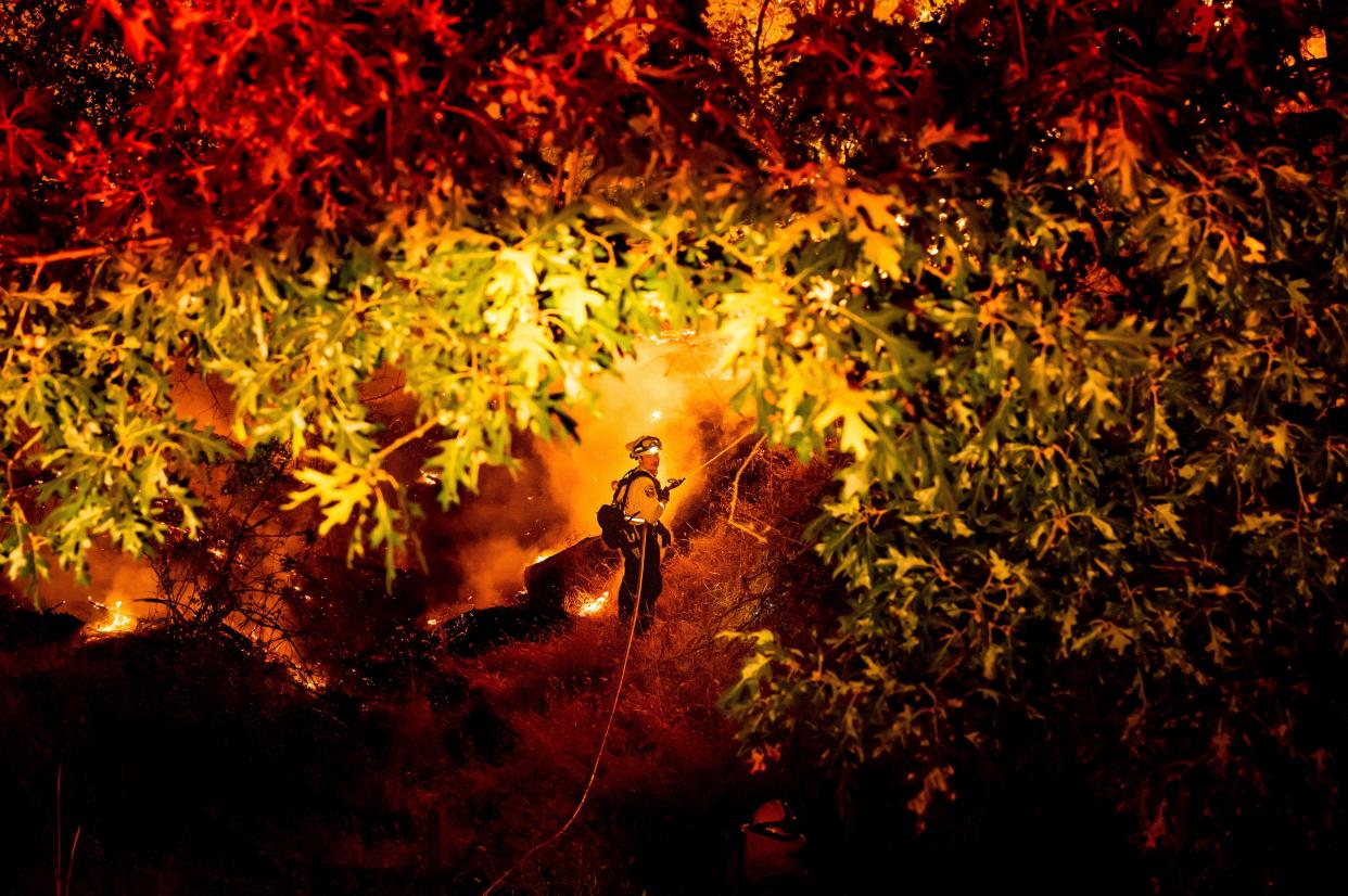 A firefighter sprays water on the Electra Fire burning in the Rich Gulch community of Calaveras County, Calif., on Monday, July 4, 2022. According to Amador County Sheriff Gary Redman, approximately 100 people sheltered at a Pacific Gas & Electric facility before being evacuated in the evening.