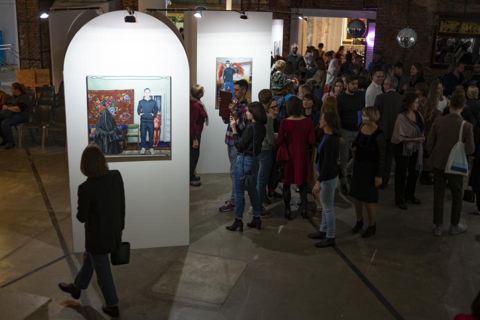 In this photo taken on Saturday, Oct. 26, 2019, visitors look at the works showing an extreme outsider's view of Moscow reality by self-taught painter Pasmur Rachuiko, in the Gogol Center in Moscow, Russia. Moscow’s suburbs are the focus of a major international art exhibition that has just opened in the Russian capital. The exhibit uses contemporary art to explore the many hidden facets of life beyond the Russian capital’s nucleus. Austrian cultural attache says the ‘real’ Moscow where most of the city’s 12.6 million people live, is outside the center. (AP Photo/Alexander Zemlianichenko)