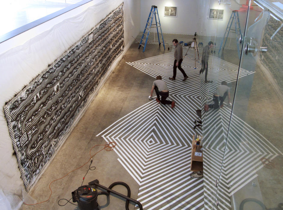 In this Tuesday, Feb. 19, 2013 photo, Ryan Travis Christian, top, and assistant Travis Fish put the finishing touches on a floor installation at the Contemporary Art Museum in Raleigh, N.C. The Chicago artist completely reworked his wall-sized drawing, left, several days into his first museum exhibition. (AP Photo/Allen Breed)