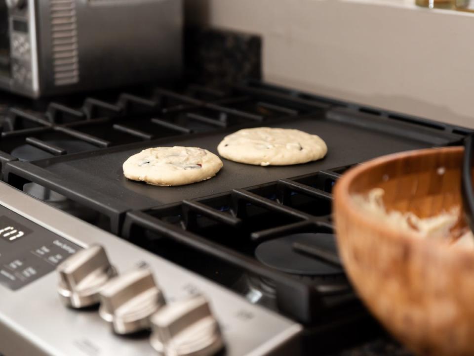 A black stovetop range with a built-in griddle and two uncooked pancakes on top