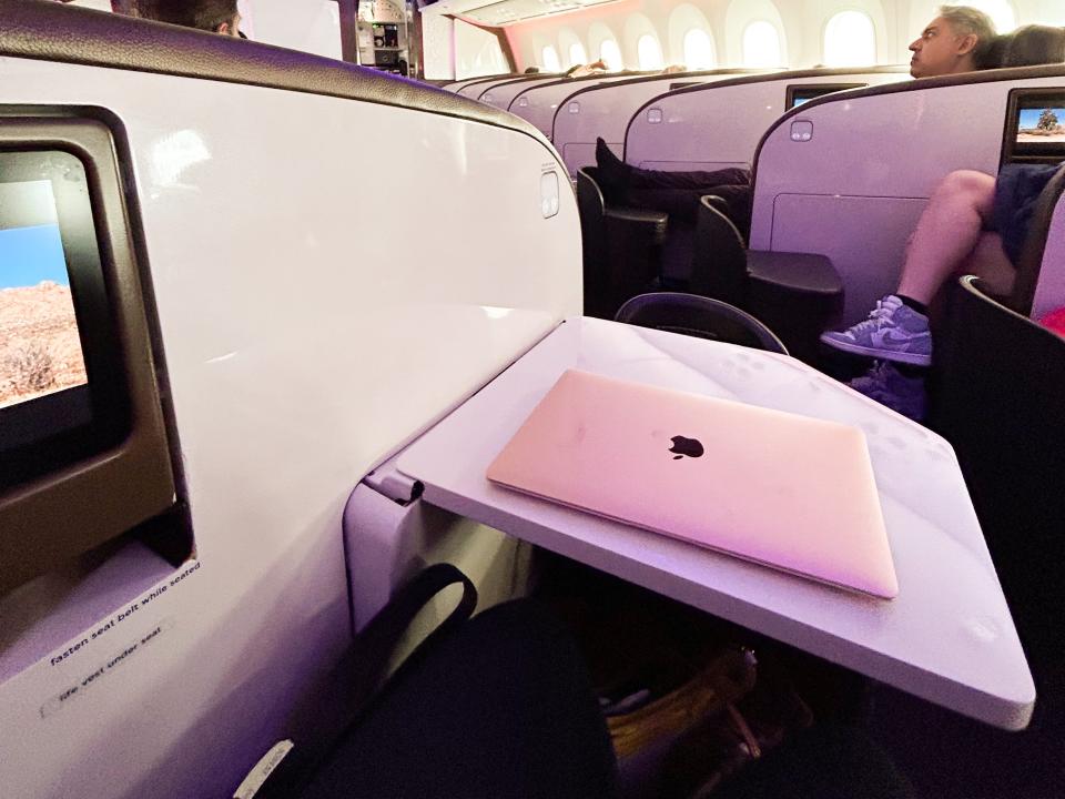 An Apple laptop on a spacious desk in business-class.