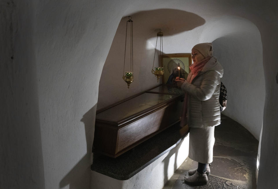 A believer holds a candle as she prays at a sarcophagus with holy relics in the underground labyrinth of the Monastery of the Caves, also known as Kyiv-Pechersk Lavra, one of the holiest sites of Eastern Orthodox Christians, in Kyiv, Ukraine, Friday, March 24, 2023. Tensions are on the rise at a prominent Orthodox monastery in Kyiv where the monks are facing eviction later this month. The Ukrainian government accuses the monks of links to Moscow, even though they claim to have severed ties with the Russian Orthodox Church following Russia's full-scale of invasion of Ukraine. (AP Photo/Efrem Lukatsky)