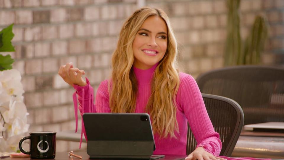 Chrishell Stause wearing a Barbie pink knit while working on her iPad in Selling Sunset 