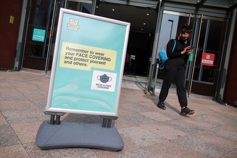 A woman wearing a protective mask walks near an informational poster, in Warrington