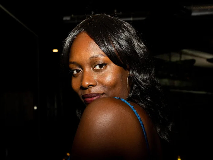 Kiana Tiese, a Black woman in a blue tank top, looks over her shoulder while smiling.