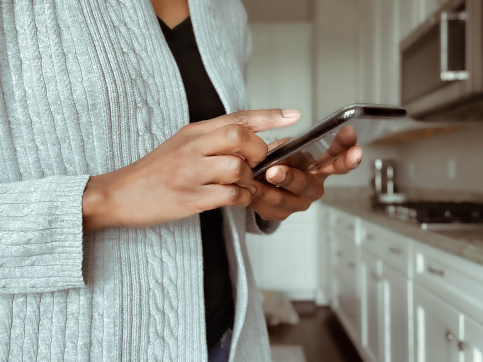 A woman taps on her phone while standing in her kitchen