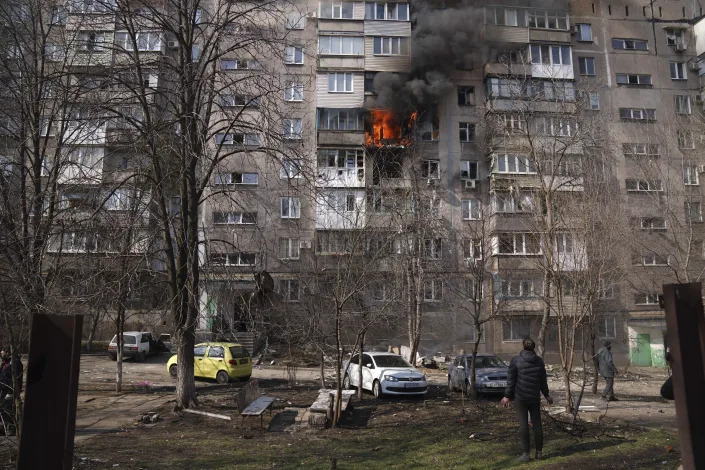 FILE - People look at a burning apartment building in a yard after shelling in Mariupol, Ukraine, Sunday, March 13, 2022. Since March 1, the Russian military has pummeled Mariupol with fierce artillery barrages and air raids that have flattened most of what once was a bustling seaside city. (AP Photo/Evgeniy Maloletka, File)