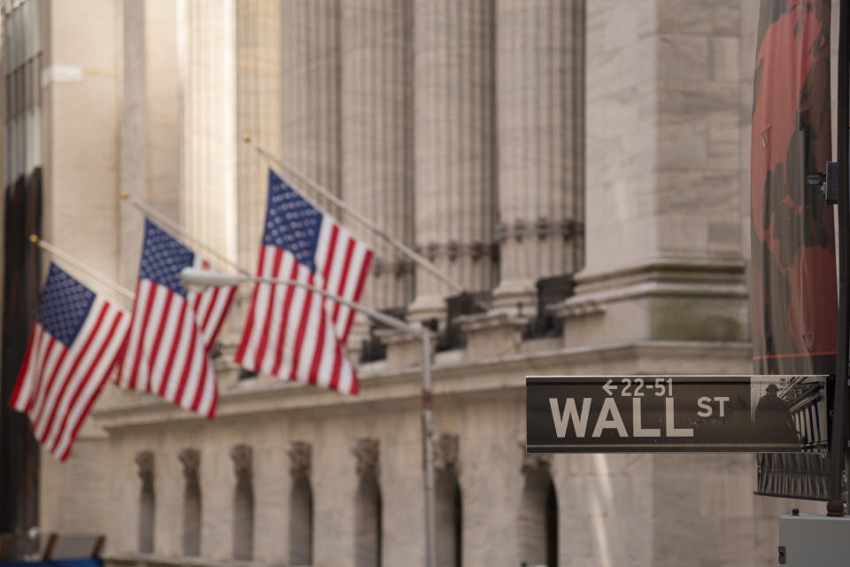 A Wall St. street sign with a building and American flags in the background.