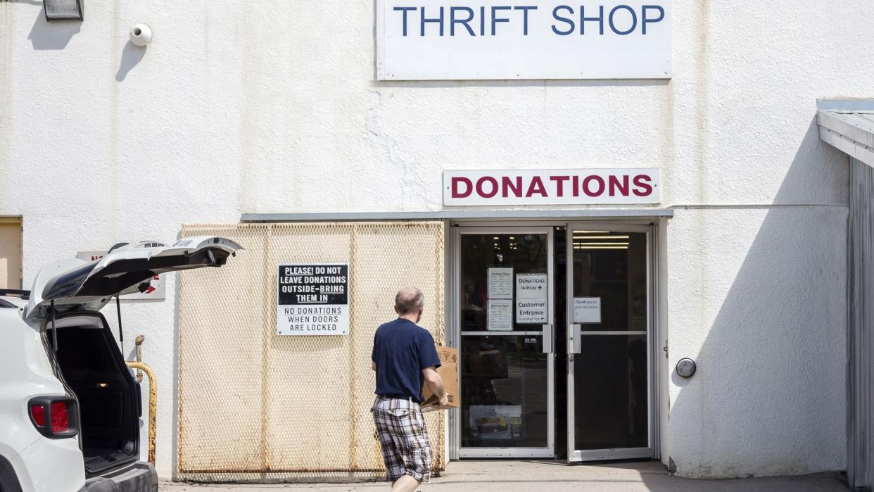 horizontal image of a man carrying donated items into a thrift store .