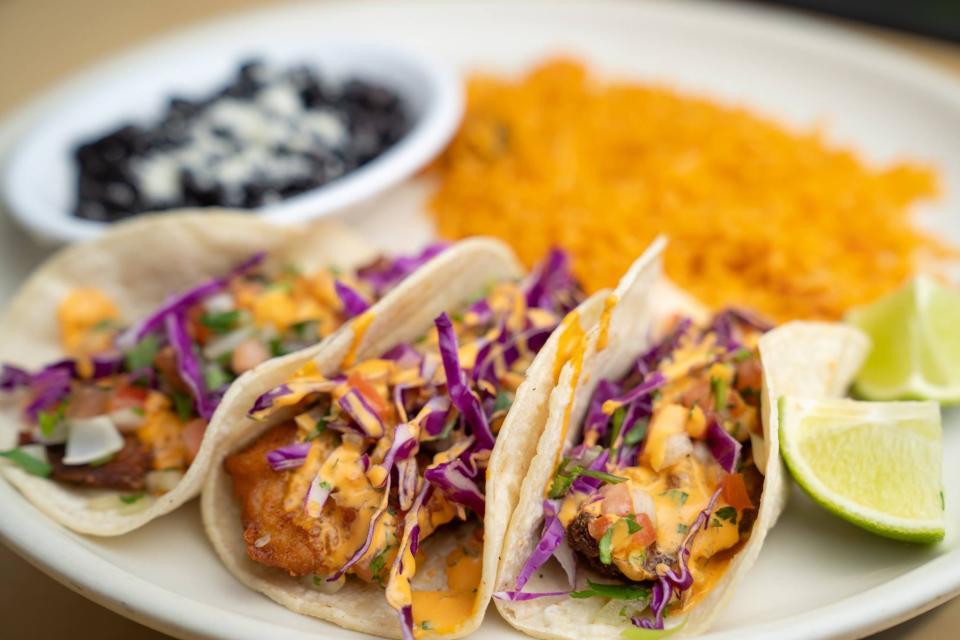 Baja Fish Tacos are a seafood special at Fiesta Mexican Restaurant, with three fried tilapia tacos on a soft corn tortilla, topped with red cabbage, pico de gallo, and chipotle sauce, served with Mexican rice and black beans.