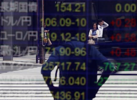 FILE PHOTO: Passersby are reflected on an electronic board showing the exchange rates between the Japanese yen and the U.S. dollar and other market indices outside a brokerage in Tokyo