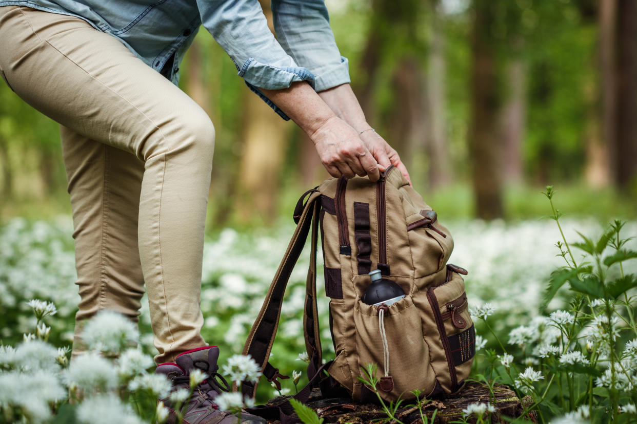 Female explorer opening backpack during hiking in spring forest. Woodland with flowers. Exploration and adventure in nature