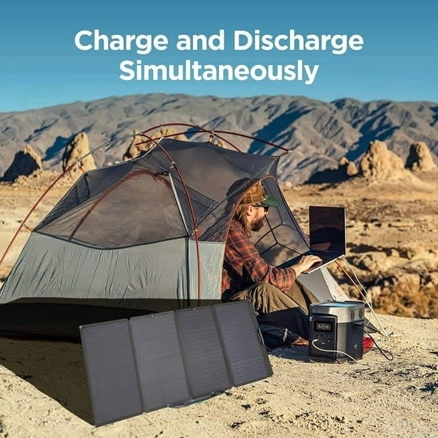 Person using a portable power station and solar panels while camping in the desert. Text: Charge and Discharge Simultaneously