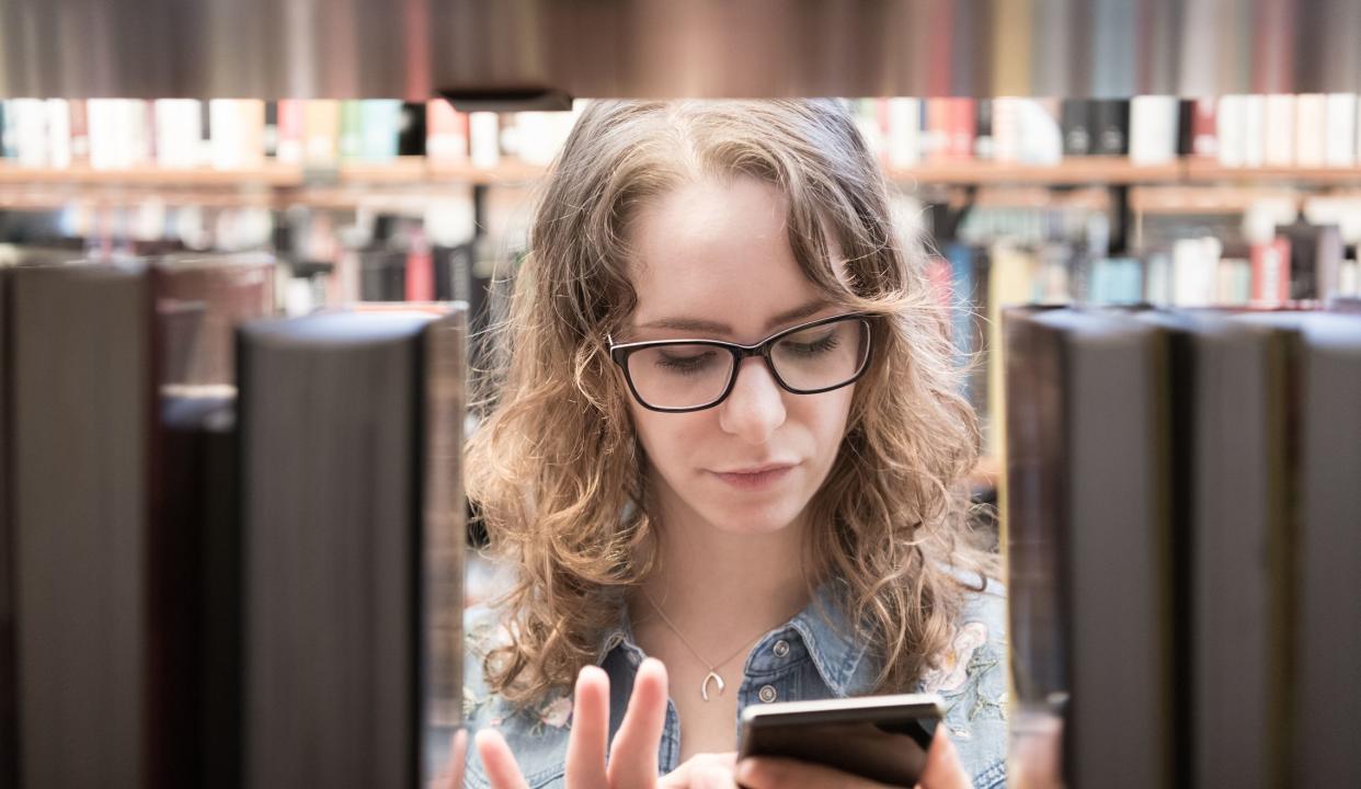 Student with glasses using mobile phone in library