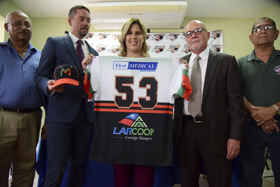 La primera base e integrante de la selección nacional de béisbol de mujeres de Puerto Rico, Diamilette Quiles Alicea, centro, posa en su presentación como la primera jugadora en firmar con los Montañeses de Utuado, uno de los equipos de la Liga Superior Doble A, en San Juan, Puerto Rico, el jueves 16 de mayo de 2019. Quiles aparece acompañada por el director ejecutivo de la Liga, Pedro Vargas, izquierda; el manager de los Montañeses, Rafael Juarbe, segundo de izquierda a derecha, el presidente de la Federación, el doctor José Quiles Rosas, segundo de derecha a izquierda, y el directior ejecutivo de la Liga de Béisbol Femenino, José Rafael Torres. (AP Foto/Carlos Giusti)