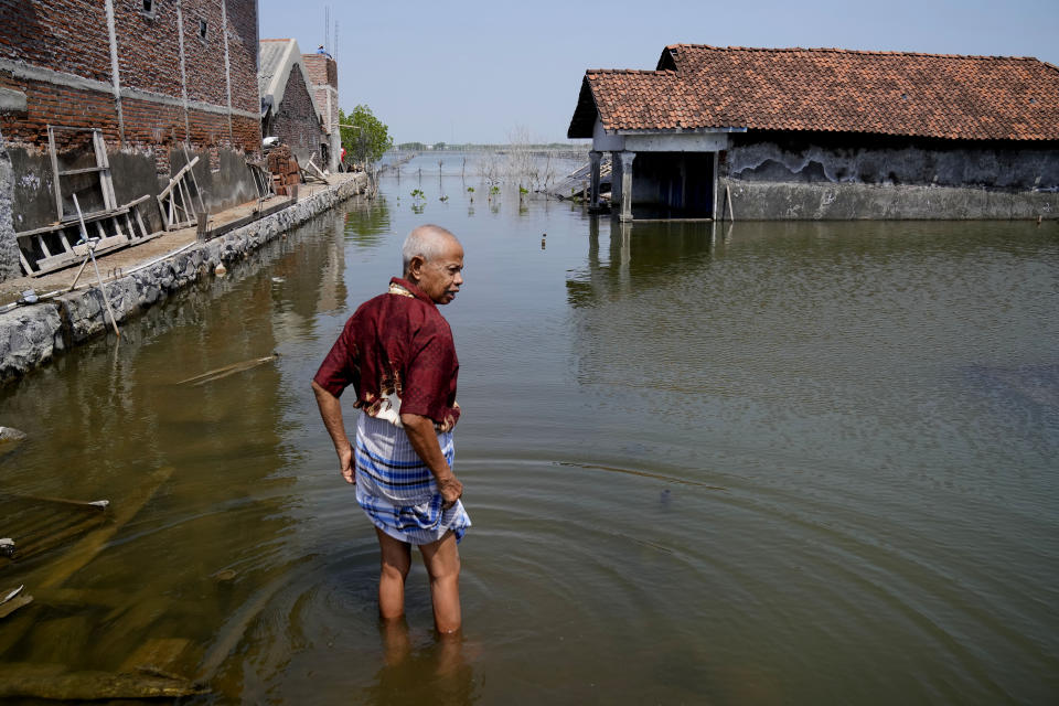 Sukarman walks on a flooded pathway outside his house in Timbulsloko, Central Java, Indonesia, Saturday, July 30, 2022. Sukarman thinks younger people, such as his granddaughter Dwi Ulfani, should try to move out of the village if they can. But he's resigned to the fact that with no money or other family homes, he's likely to spend the rest of his life living in an increasingly flooded home. (AP Photo/Dita Alangkara)