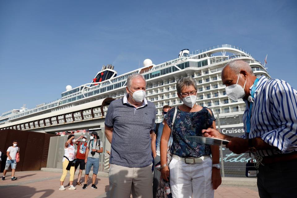 This image shows two people looking at a piece of paper another person is holding in front of a cruise ship.