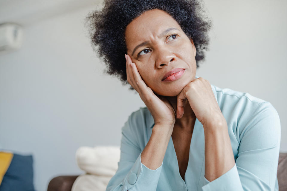 A person with a thoughtful expression, resting their head on their hand while wearing a light-colored shirt. Their gaze is directed to the side