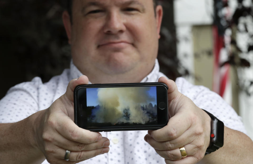 In this photo taken Friday, Aug. 2, 2019, Jason Ritchie holds his phone with a photo he took of a wildfire behind his home four years earlier, in Sammamish, Wash. (AP Photo/Elaine Thompson)