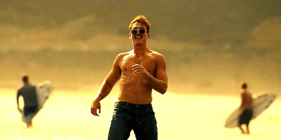 Miles Teller shirtless with sunglasses on smiling on a beach