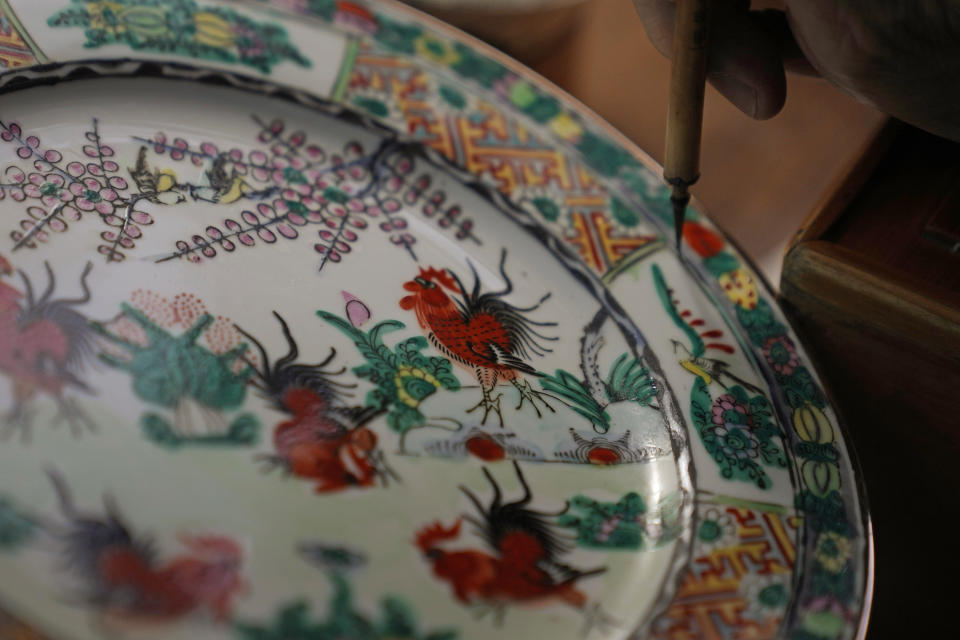 Joseph Tso, owner of Yuet Tung China Works, Hong Kong's last hand-painted porcelain factory, re-paints an old porcelain in Hong Kong, Wednesday, June 8, 2022. The traditional technique of painting “guangcai,” or Canton porcelain is a fading art in this modern metropolis, as fewer young people are willing to put in the time and effort required to master the craft or to work at the factory full-time.(AP Photo/Kin Cheung)