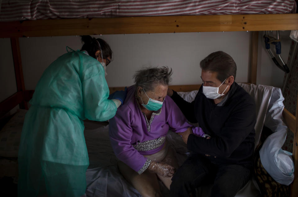 A home care doctor performs a physical exam on Felicidad while her son, Joan, holds her arm at her home in Barcelona, Spain, March 31, 2020. Felicidad had been admitted to the hospital after suffering a stroke but was sent home within a day and soon developed respiratory symptoms. (AP Photo/Emilio Morenatti)