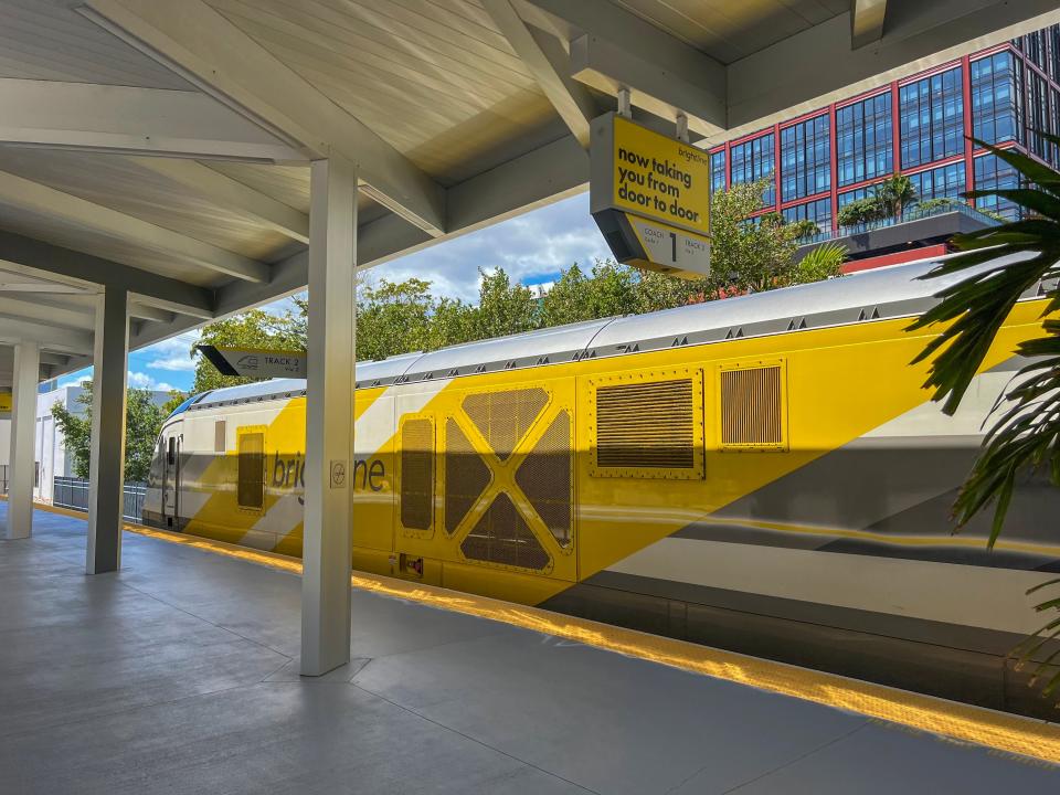A yellow Brightline train is shown at a station.