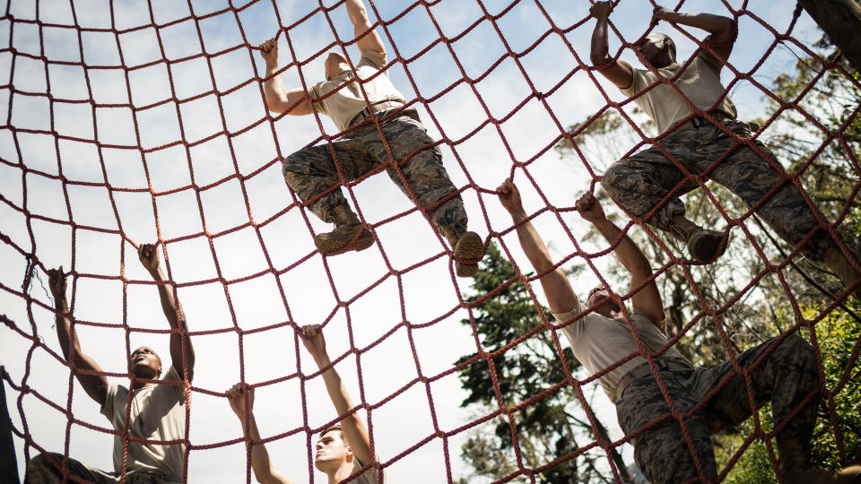 soldiers climbing rope during obstacle course in boot camp
