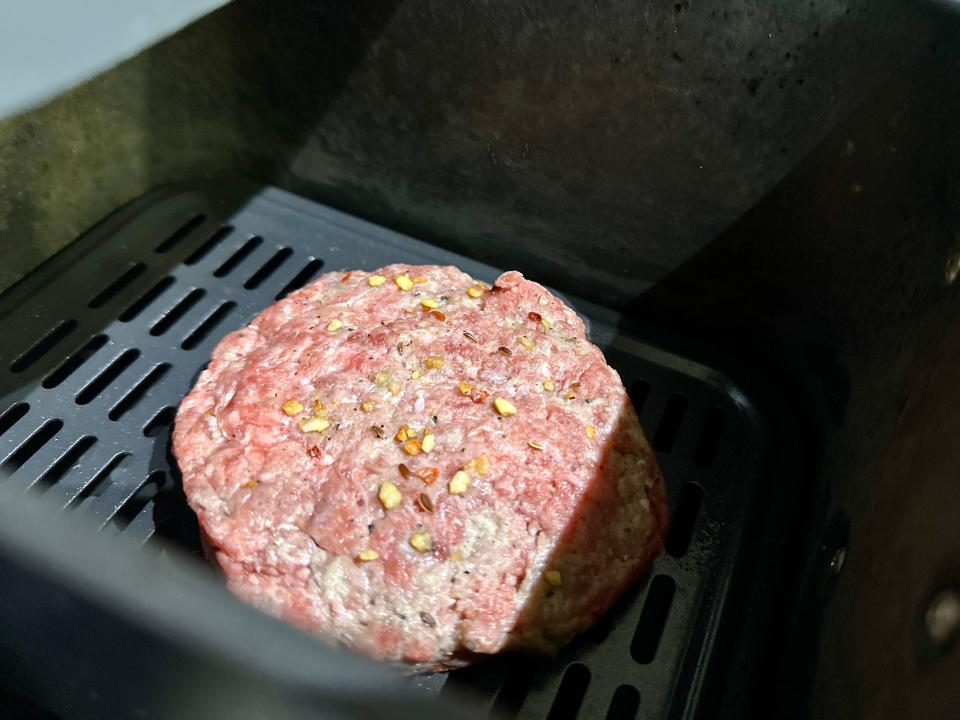 raw burger patty in an air fryer basket