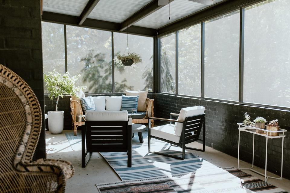 Sunroom painted black with chairs and layered rugs