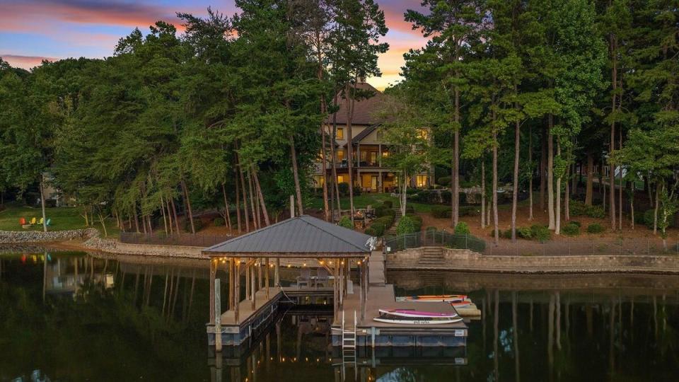 a house on a dock surrounded by water with trees and a building in the background