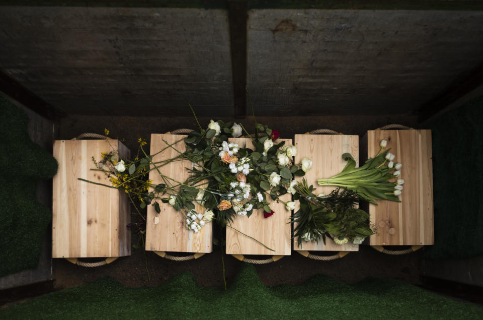 Flowers on caskets containing bones found on the grounds of the Freie Universitat, Free University after being lowered into the ground for burial, at the Waldfriedhof in Berlin, Germany, Thursday, March 23, 2023. Thousands of bone fragments found in the grounds of a Berlin university where an institute for anthropology and eugenics was once located, which may include the remains of victims of Nazi crimes, were buried on Thursday. (AP Photo/Markus Schreiber)