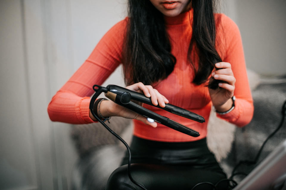 young brunette long haired teenager using hair straightener