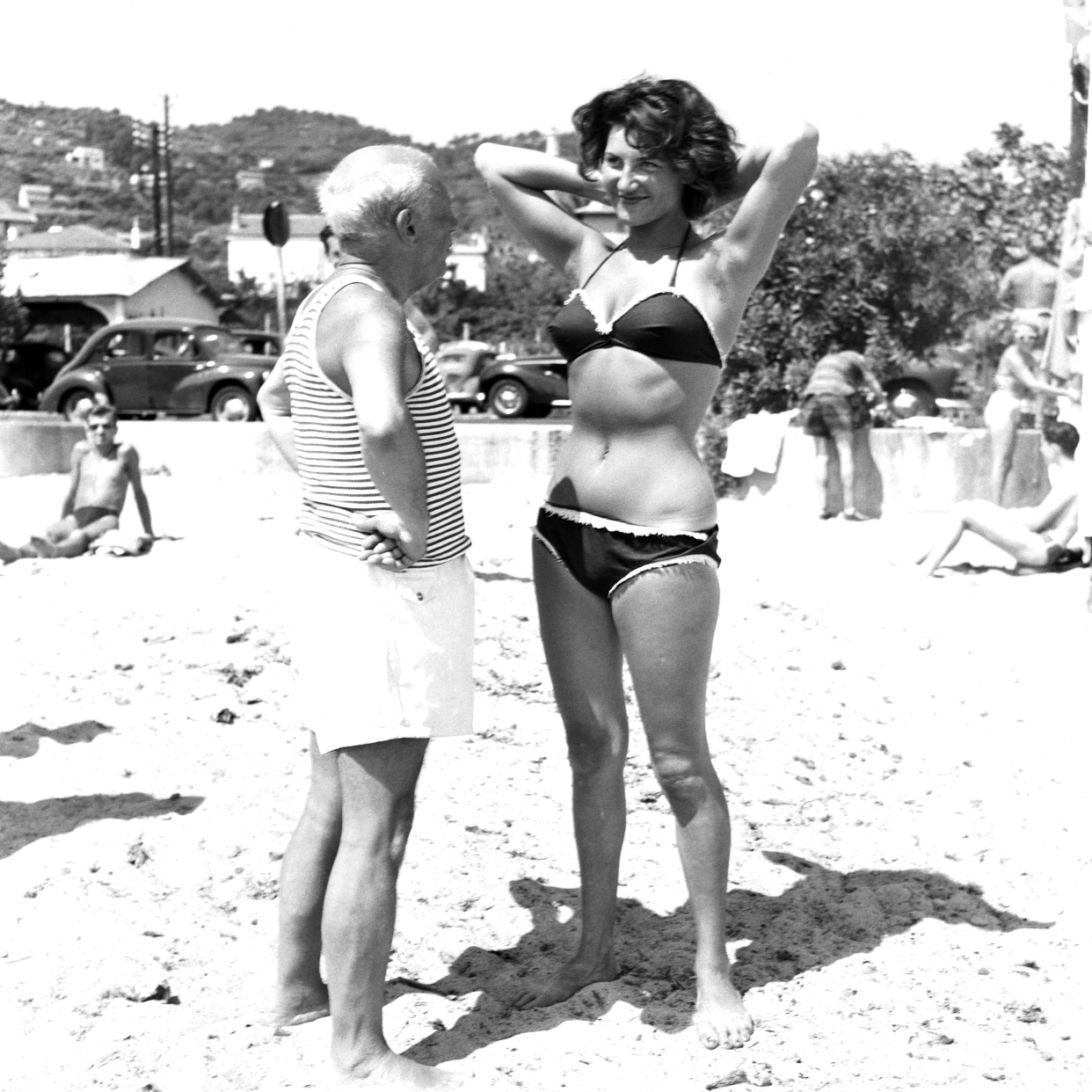 Spanish painter Pablo Picasso makes a young woman wearing a bikini smile on the beach at Golfe Juan on the Riviera, Vallauris, France