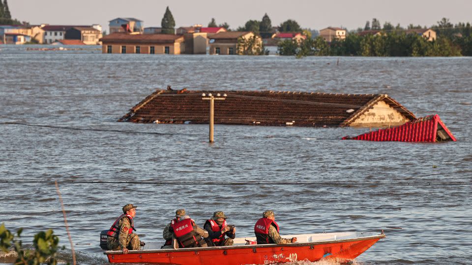 Rescue workers ride past the roof of an inundated house following a dam breach at Hunan province's Dongting Lake on July 7. - AFP/Getty Images