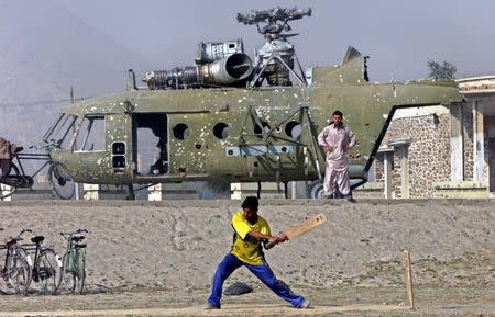 A young Afghan plays cricket near a war-damaged Soviet helicopter in Kabul October 25, 2002. REUTERS/Bazuki Muhammad/Files