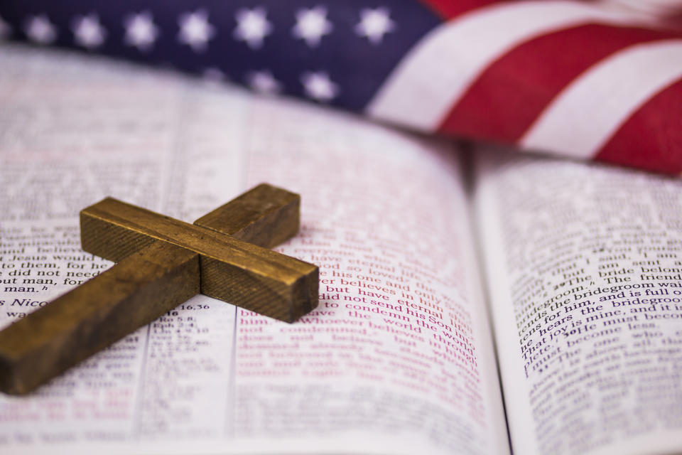 A small wooden cross and American flag rest on an open page of a book.