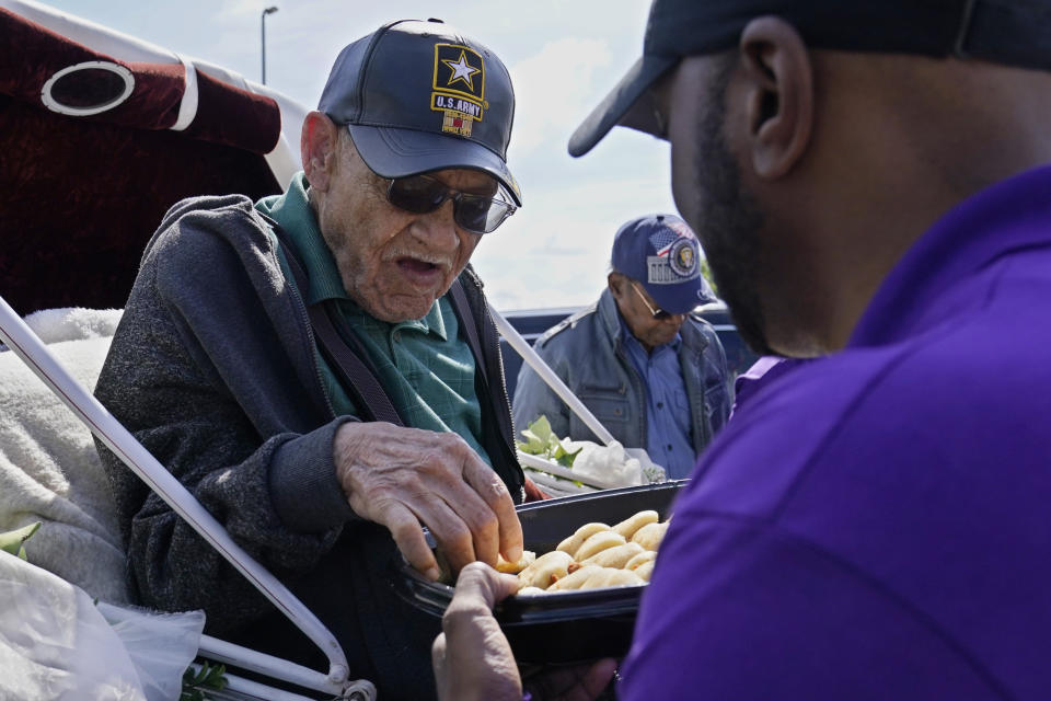FILE - Hughes Van Ellis, a Tulsa Race Massacre survivor and World War II veteran, left, takes a pastry from a tray held by attorney Damario Solomon-Simmons, right, as he waits in a horse-drawn carriage for a protest march, May 28, 2021, in Tulsa, Okla. Van Ellis, who was the youngest known survivor of the Tulsa Race Massacre and who spent his latter years pursuing justice for his family and other descendants of the attack on “Black Wall Street,” died on Monday, Oct. 9, 2023. He was 102. (AP Photo/Sue Ogrocki, File)