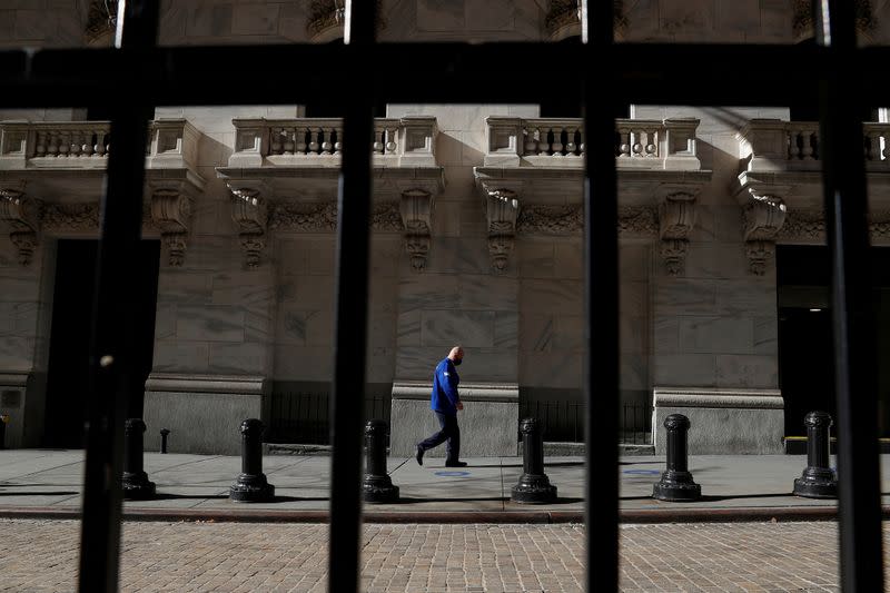 FILE PHOTO: A trader wearing a protective face mask walks, as the global outbreak of the coronavirus disease (COVID-19) continues, at the New York Stock Exchange (NYSE) in the financial district of New York