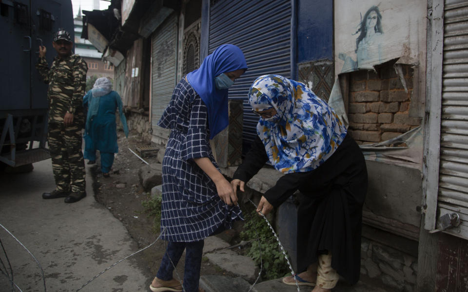 A Kashmiri woman helps another woman untangle her clothes caught in a barbwire put up by Indian security forces as a roadblock during restrictions in Srinagar, Indian controlled Kashmir, Friday, Aug. 28, 2020. Police and paramilitary soldiers on Friday detained dozens of Muslims participating in religious processions in the Indian portion of Kashmir. Authorities had imposed restrictions in parts of Srinagar, the region's main city, to prevent gatherings marking Muharram from developing into anti-India protests. (AP Photo/Mukhtar Khan)