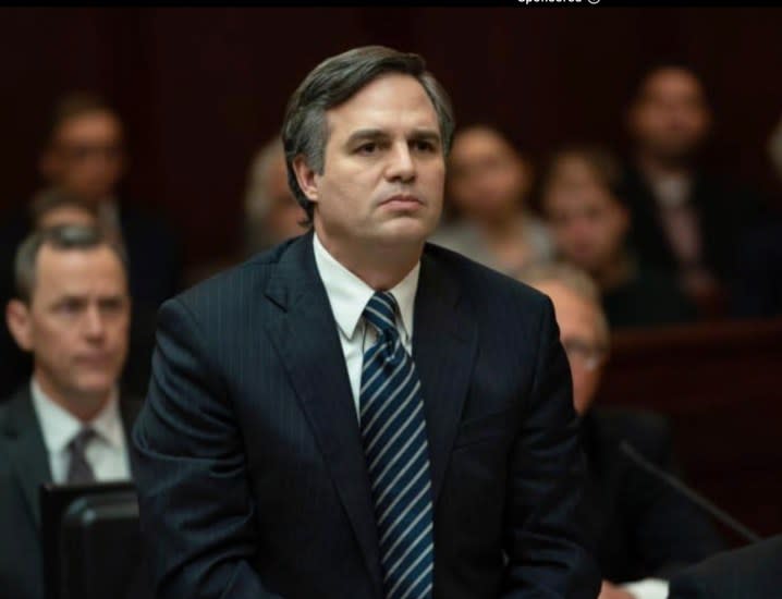 A man stands behind a table while wearing a suit.