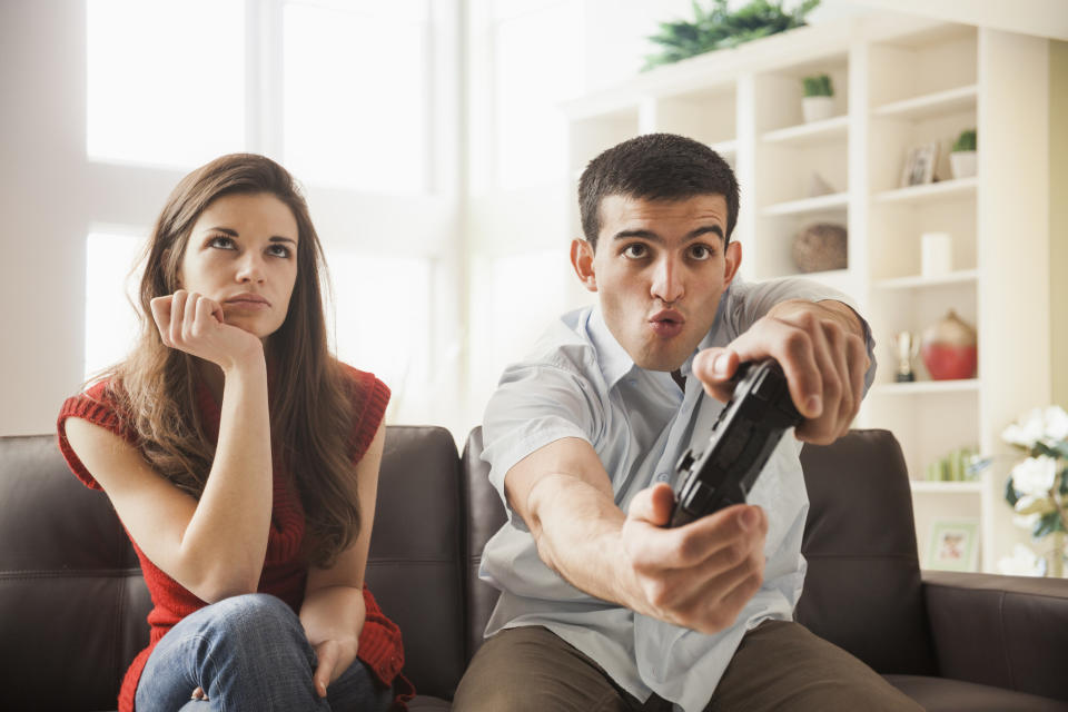 A woman sitting bored while her significant other plays video games