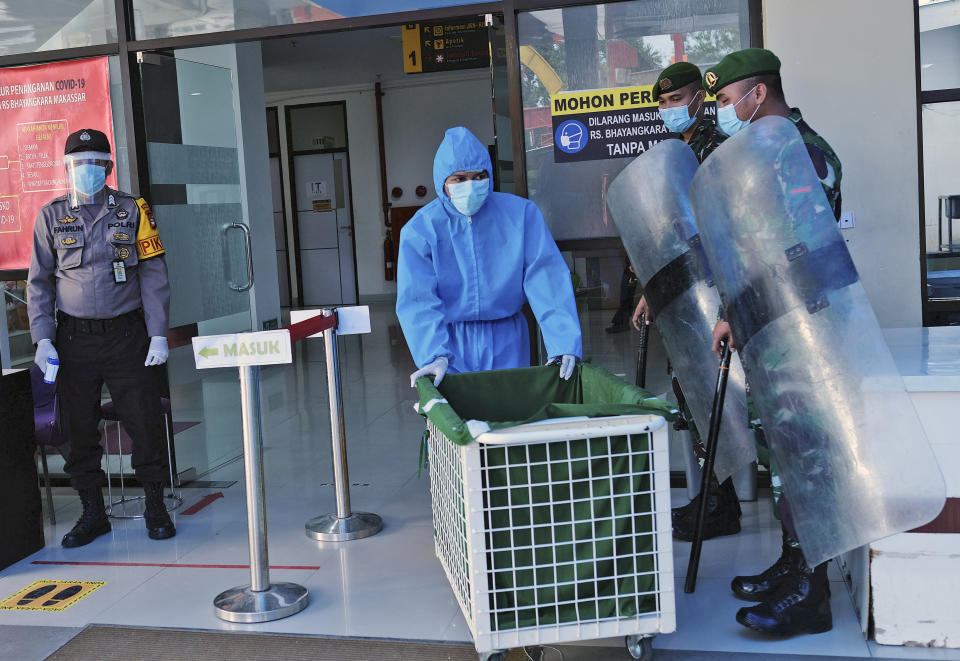 A staff member in protective suit walks past a police officer and soldiers equipped with riot gears who are stationed at Bhayangkara Hospital following an incident where mob forcefully took the body of a man who presumably died of COVID-19, in Makassar, South Sulawesi, Indonesia, Sunday, June 21, 2020. As Indonesia’s virus death toll rises, the world’s most populous Muslim country finds itself at odds with protocols put in place by the government to handle the bodies of victims of the pandemic. This has led to increasing incidents of bodies being taken from hospitals, rejection of COVID-19 health and safety procedures, and what some experts say is a lack of communication from the government. (AP Photo/Masyudi Syachban Firmansyah)