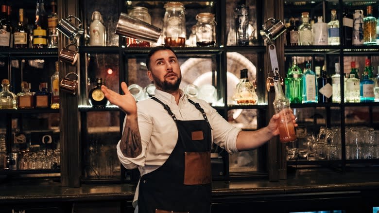 A bartender juggling cups and shakers behind a bar