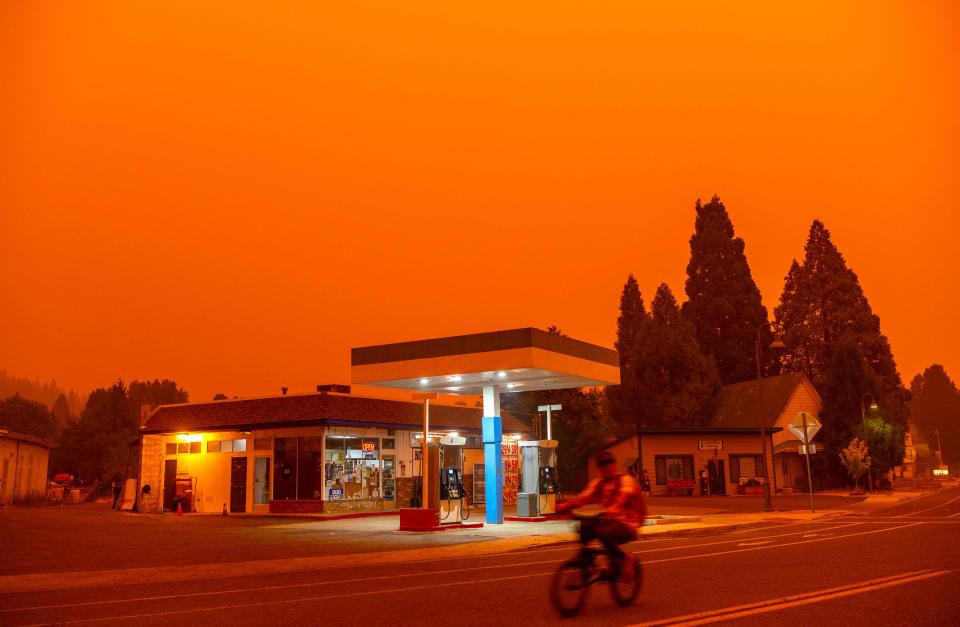 A man rides his bike passed a gas station as smoke fills the sky during the Dixie fire in Greenville, California on July 23, 2021. 