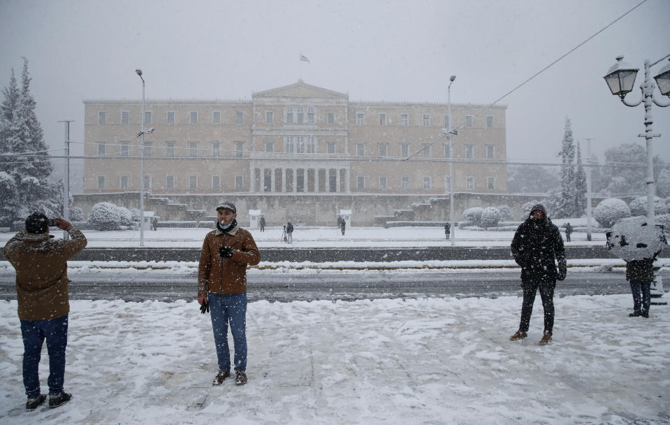 People take photographs as snow falls in front of the Greek parliament in Athens, Tuesday, Feb.16, 2021. A cold weather front has hit Greece, sending temperatures plunging from the low 20s Celsius (around 70 Fahrenheit) on Friday to well below freezing on Tuesday, and heavy snowfall in central Athens. (AP Photo/Thanassis Stavrakis)