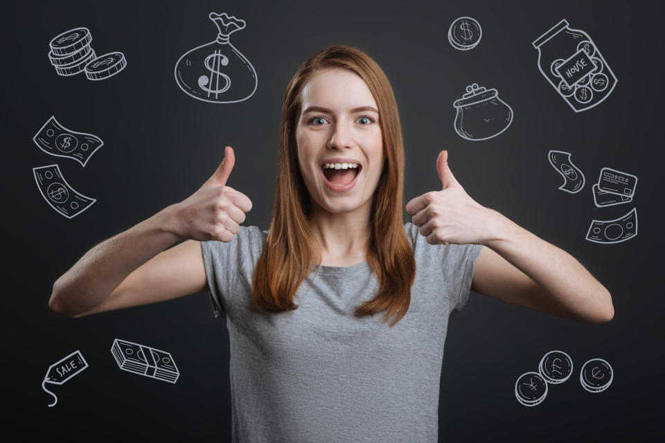 Young woman with thumbs up in front of a chalkboard with drawings of money