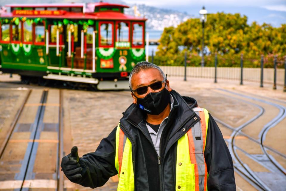 A man stands in front of a cable car at the turnaround overlooking the San Francisco Bay