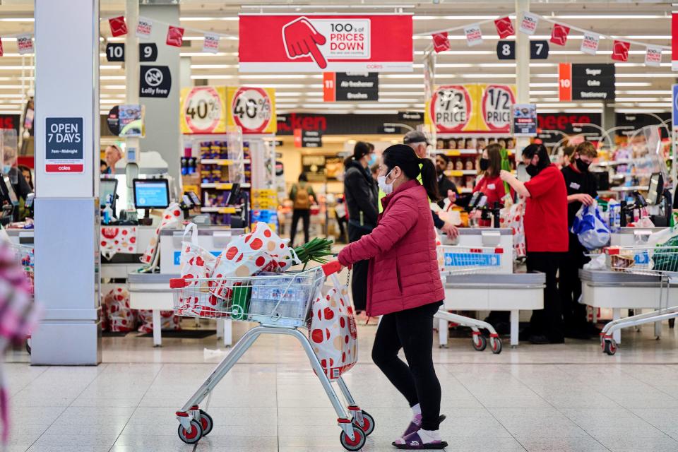 Woman pushing trolley past Coles storefront