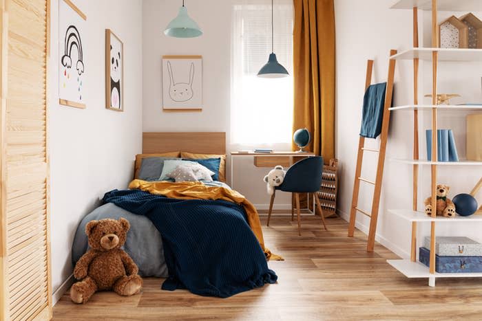 Cozy children's bedroom with wooden furniture, teddy bear on floor, art on walls, and bright mustard curtains